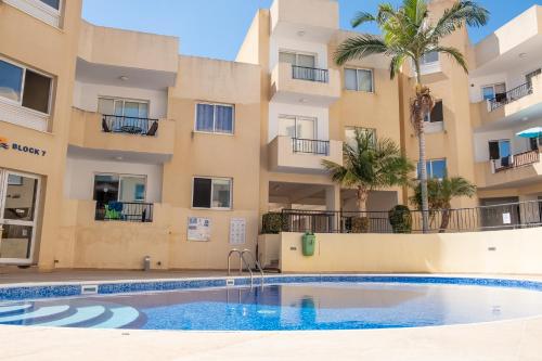 a swimming pool in front of a building with palm trees at Stylish 2 Bedroom apartment in Pegia in Peyia
