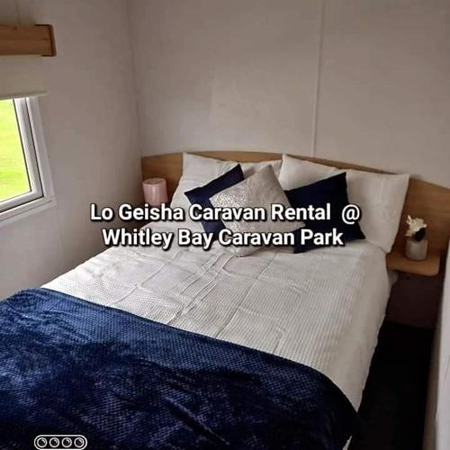 a bedroom with a bed with blue and white pillows at Lo Geisha Caravan Rental at Whitley Bay Caravan Park in Whitley Bay