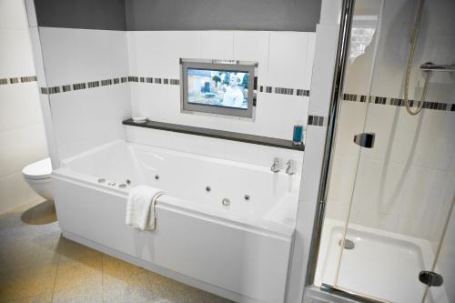 a white bathroom with a tub and a tv on the wall at Judges Hotel in Yarm