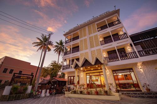 a white building with a palm tree in front of it at LuangPrabang Center Hotel in Luang Prabang