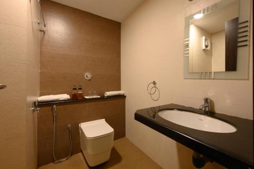 a bathroom with a sink and a toilet and a mirror at Hotel Samudyatha Inn And Suites in Kundapur