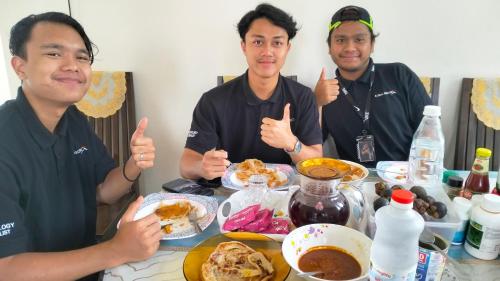 three men giving thumbs up while sitting at a table with food at Homestay Dena Moon Inn in Tumpat