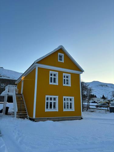een geel huis met sneeuw ervoor bij Curry house rooms in Seyðisfjörður