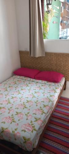 a bed with a floral comforter and a window at Suítes Família Mateus in Ubatuba