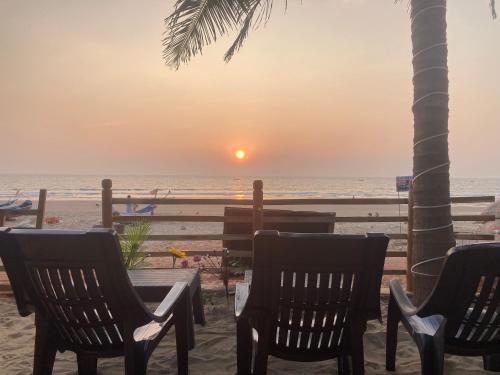 a table and chairs on the beach with the sunset at Oceanic Stay And Restaurant Gokarna in Gokarn
