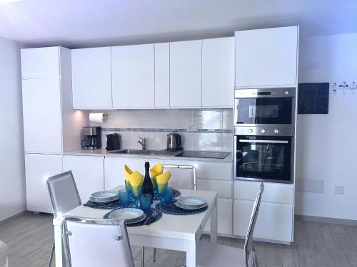 a white kitchen with a table with plates and chairs at Alloggio Ulivi in Isola Rossa