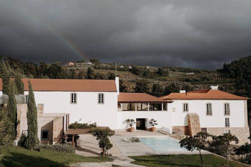 a large white house with a rainbow in the background at Quinta do Pinhô - The Poolhouse in Salzedas
