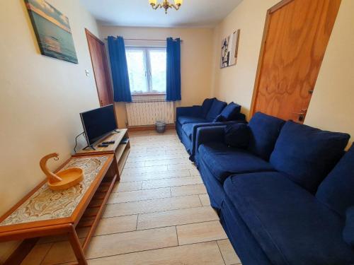 a living room with a blue couch and a television at Mas Des Sables Seaside Cottages in Grandes Rocques
