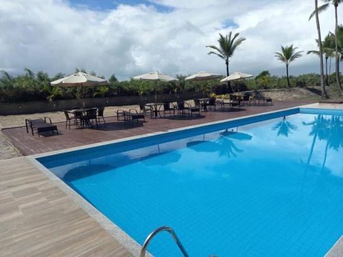 uma grande piscina azul com mesas e guarda-sóis em Condomí. Praia da Pérola -Beira Mar-Ilhéus/Itacaré em Ilhéus