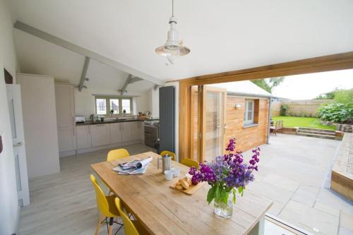 a kitchen and dining room with a wooden table and flowers at Barnwell Cottage *Stunning Cornish Cottage* Oozing Charm + Comfort in Cubert