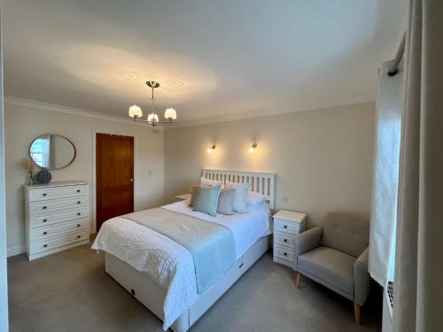 a white bedroom with a bed and a chair at Rhos Helyg - Beach-side luxury stylish house in Aberaeron
