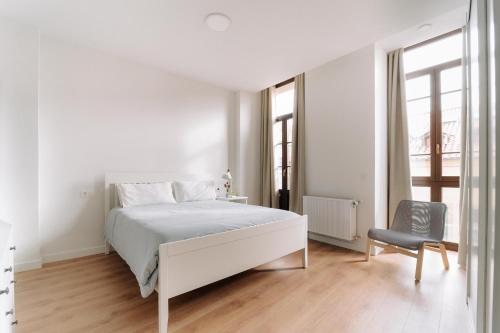 a white bedroom with a white bed and a chair at San Bernardo, 19 in Avilés