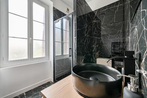 La salle de bains est pourvue d'une baignoire noire et d'un lavabo. dans l'établissement Ptit Villemomble - Wifi - Paris & Disney, à Villemomble