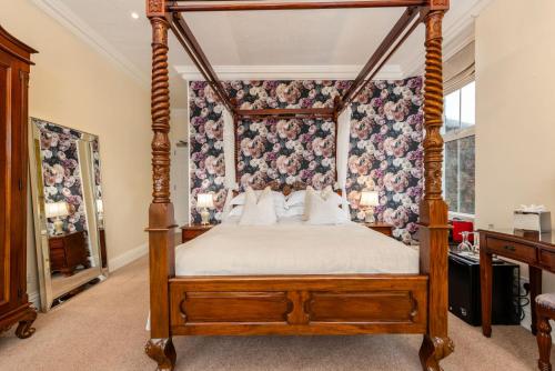 a four poster canopy bed in a bedroom with floral wallpaper at Wheatlands Lodge-Windermere - Award Winning - Adult Only - Car Park in Windermere