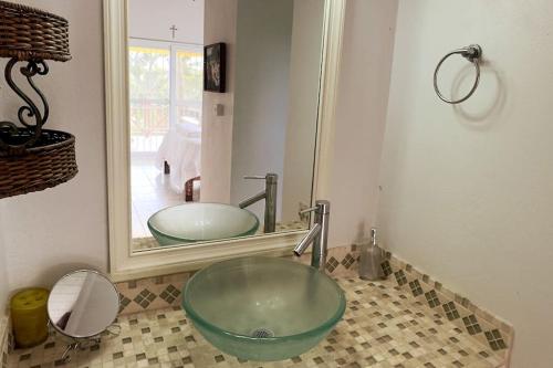 uma casa de banho com um lavatório de vidro em frente a um espelho em LaCaye - Home in Creole em Calibishie