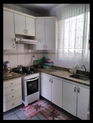a kitchen with white cabinets and a sink and a stove at Quarto solteiro Praia de Camburi in Vitória