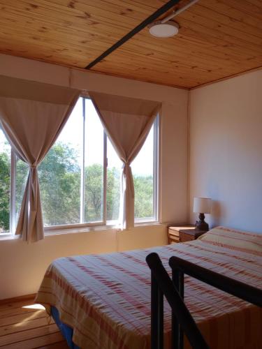 a bedroom with a bed and two large windows at Cabañas Guayacán in Bialet Massé