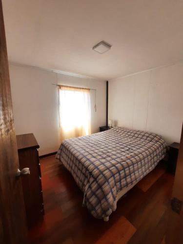 1 dormitorio con 1 cama con manta a cuadros y ventana en Cabaña, en Pichidangui