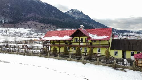 a yellow building with a red roof in the snow at Maricom Home in Zărneşti