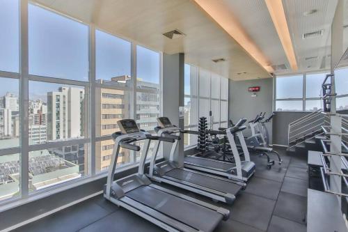 a gym with treadmills and ellipticals in a building with windows at 2 quartos c/ AC na Savassi in Belo Horizonte