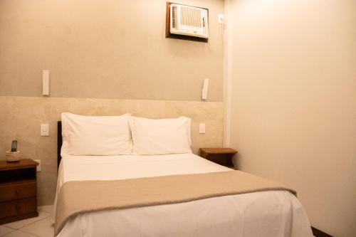 a bedroom with a bed with white sheets and a microwave at Pousada Farol dos Borbas in Abraão