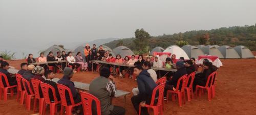 a group of people sitting in red chairs in front of tents at Yuva Yatri Campsite in Mahabaleshwar