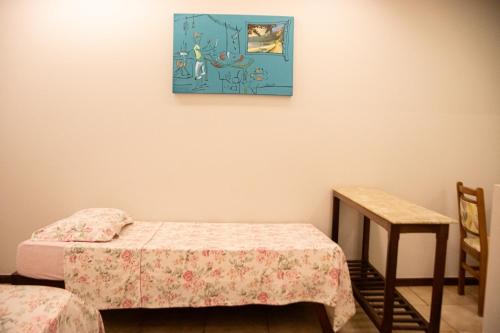 a room with a bed and a table and a painting at Pousada Farol dos Borbas in Abraão