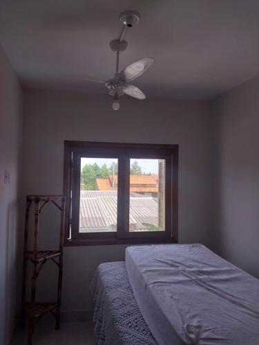 1 dormitorio con ventilador de techo y ventana en Duplex novo en Tramandaí