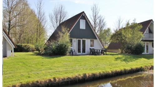 a house with a thatched roof on a lawn next to a river at Vijverzicht 218 met whirlpool in Gramsbergen