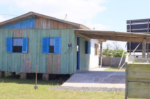 a green building with blue shutters on it at Casa de praia - Descanse e tenha uma experiencia relaxante a poucos metros da praia in Arroio do Silva