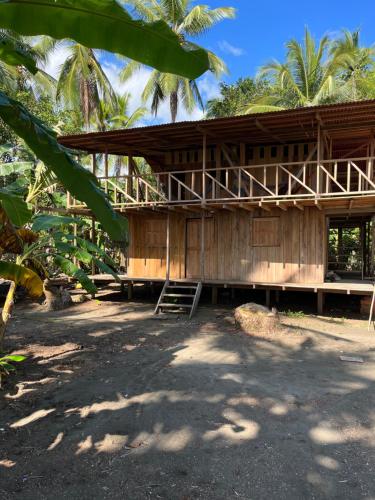 a wooden building with a porch and palm trees at Hostal San Mabel Herping - Playa Cuevita in El Valle