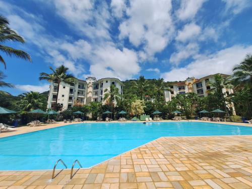 a swimming pool at a resort with palm trees and buildings at PARAÍSO Ubatuba - Praia Grande-Toninhas - Apartamento Cond Wembley Tenis in Ubatuba