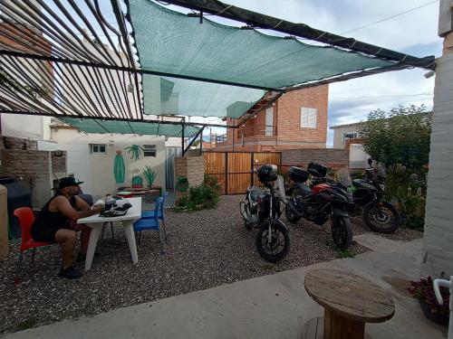 a woman sitting at a table in a backyard with motorcycles at Ruca Kiñe Hostel in Las Grutas
