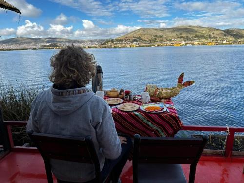 a woman sitting at a table in front of the water at Uros TITIKAKA the Best lodge in Puno
