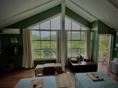 una sala de estar con paredes verdes y una gran ventana. en Jung Ja Hut, en Sai Yok
