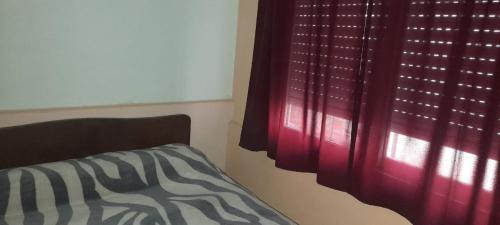 1 dormitorio con 1 cama y una ventana con cortinas rojas en Departamentos Doña Viya en Ramallo