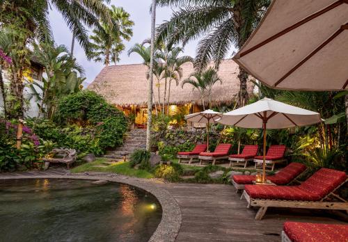 a resort with a pool with chairs and an umbrella at Stone House in Ubud