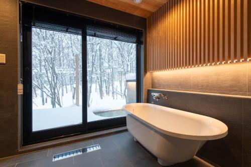a bathroom with a tub and a large window at Moraine Onsen Chalet in Niseko