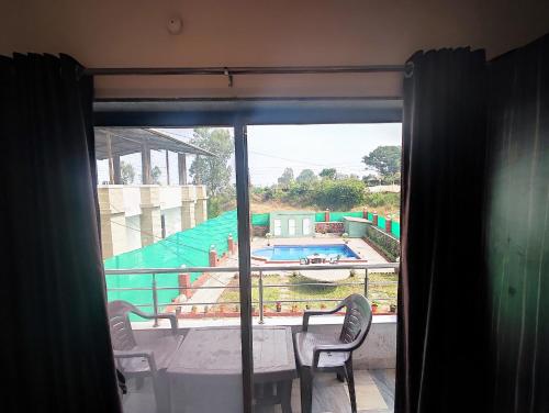 una ventana con vistas a la piscina, mesa y sillas en Hotel Oneness Palace, en Mahabaleshwar