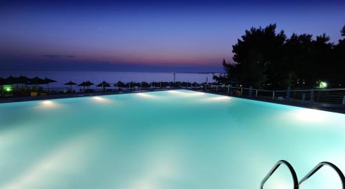 a swimming pool at night with the ocean in the background at Istion Club & Spa in Nea Potidaea