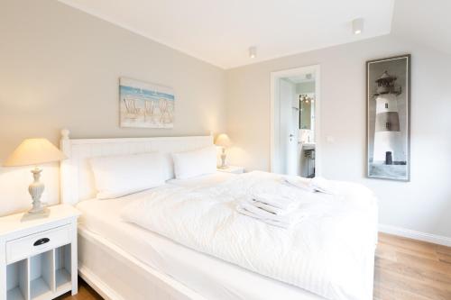 a white bedroom with a white bed and a mirror at Haus Delft Angelino in Juist