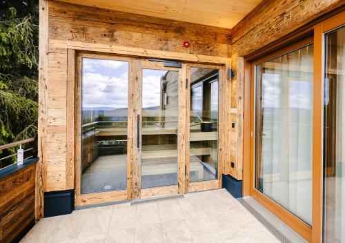 a wooden house with glass doors and a balcony at Wellnesshotel Riedlberg in Drachselsried