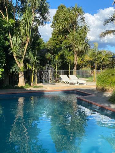 a swimming pool with a bench and palm trees at Garden Oasis in the heart of Pāpāmoa in Tauranga
