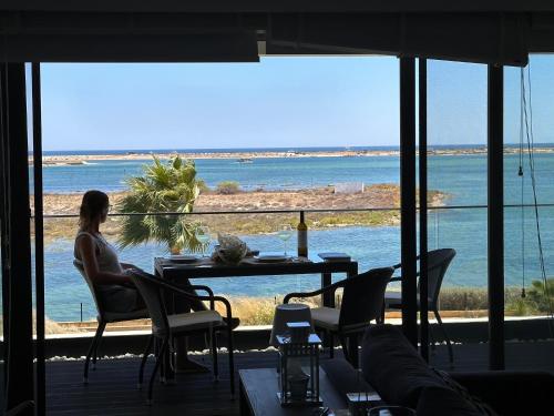 a woman sitting at a table looking out at the ocean at Fuzeta stylish 1 bedroom apartment - Amazing views in Fuzeta