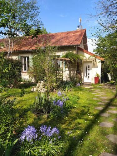 une petite maison avec une cour ornée de fleurs violettes dans l'établissement Gîte Les Lilas, à La Genevraye