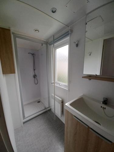 uma casa de banho branca com um chuveiro e um lavatório. em Mobil home équipé camping 5* em Houlgate