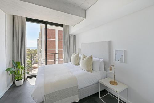 a white bedroom with a bed and a balcony at One26 On M Luxury serviced apartments - By Elevate in Cape Town