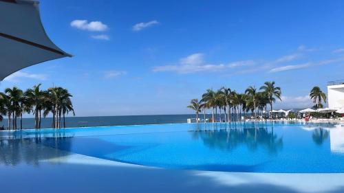 a large swimming pool with palm trees and the ocean at Semana Santa frente al mar con dos terrazas del 30 de marzo al 5 de abril Semana pascua 6 al 12 abril in Nuevo Vallarta