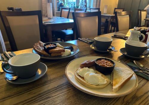 a wooden table with plates of breakfast foods and cups at The Heathfield Inn in Honiton
