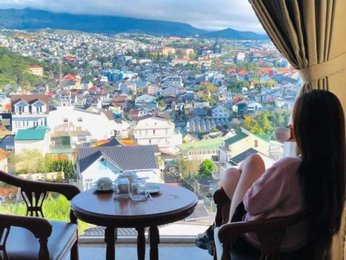 a woman sitting at a table in a window looking at a city at Cosy Hotel & Apartment Dalat in Da Lat